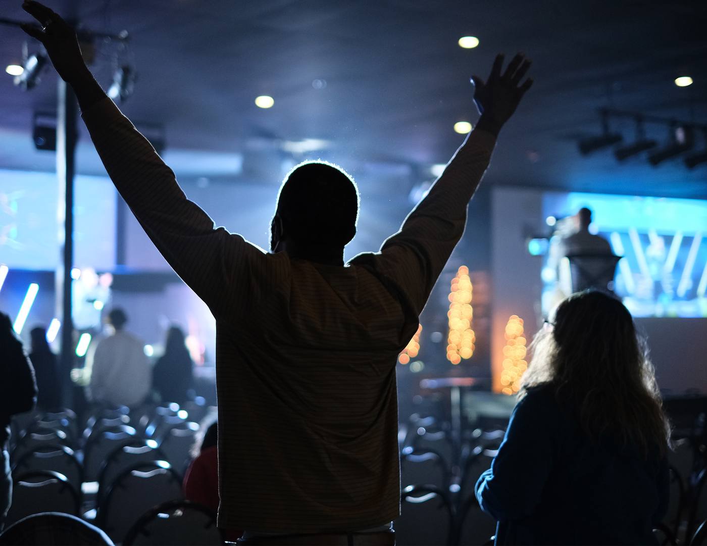 A congregation worshipping, one person with arms raised in silhouette.