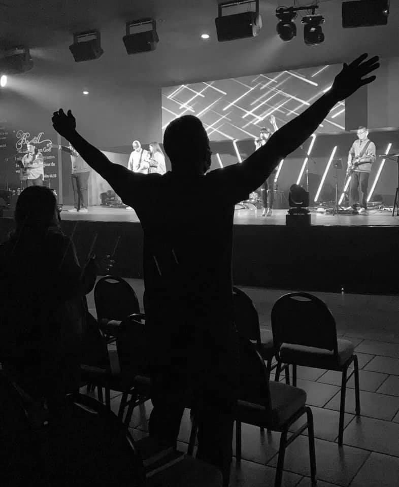 A person standing with both arms raised during worship.